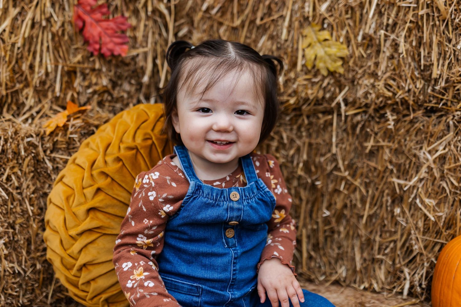 A child smiles while sitting among autumn decor and pumpkins.