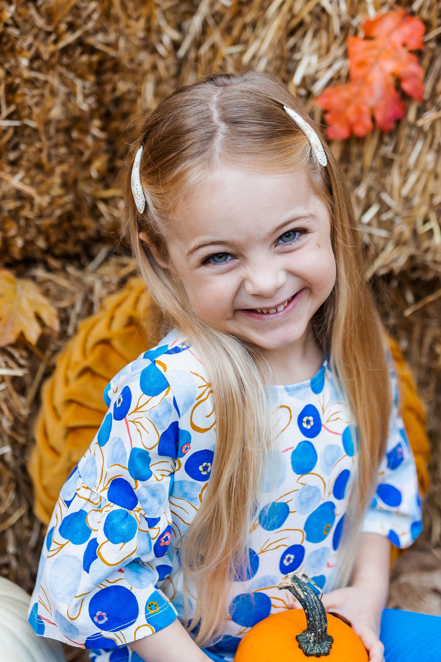 Autumn photo session with hay bales, orange pumpkins, and floral blue dress.