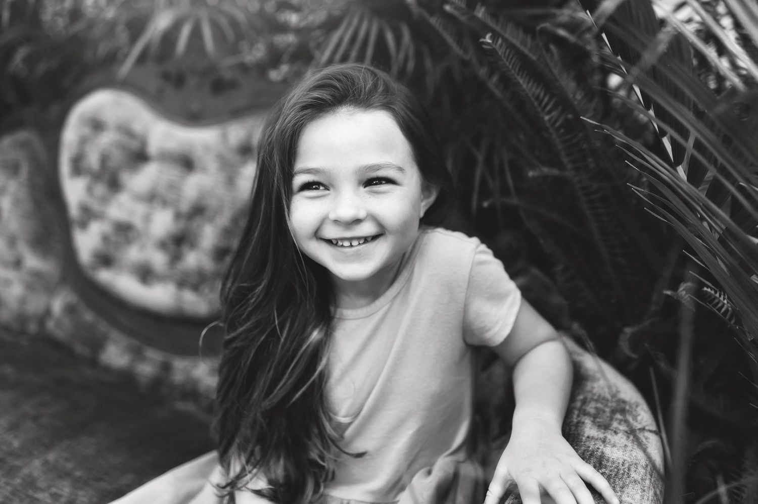 Black and white portrait of a young child smiling brightly in an outdoor setting.