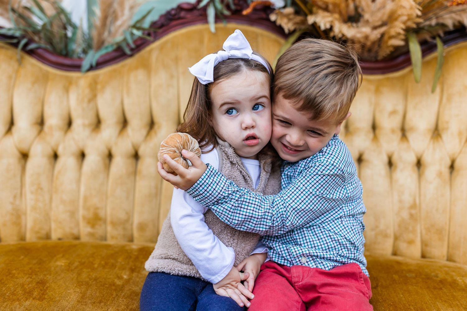 Young siblings share sweet candid moments together on a vintage gold couch with pampas grass decor.