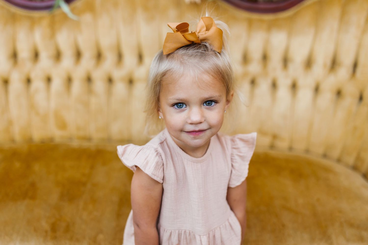 A child in a peach-colored dress sits on a vintage yellow couch.