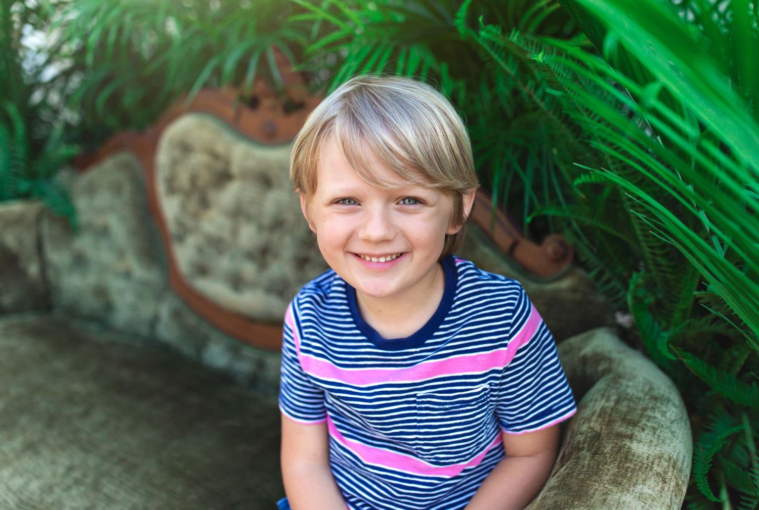Cheerful youth in striped shirt sitting among lush green plants.