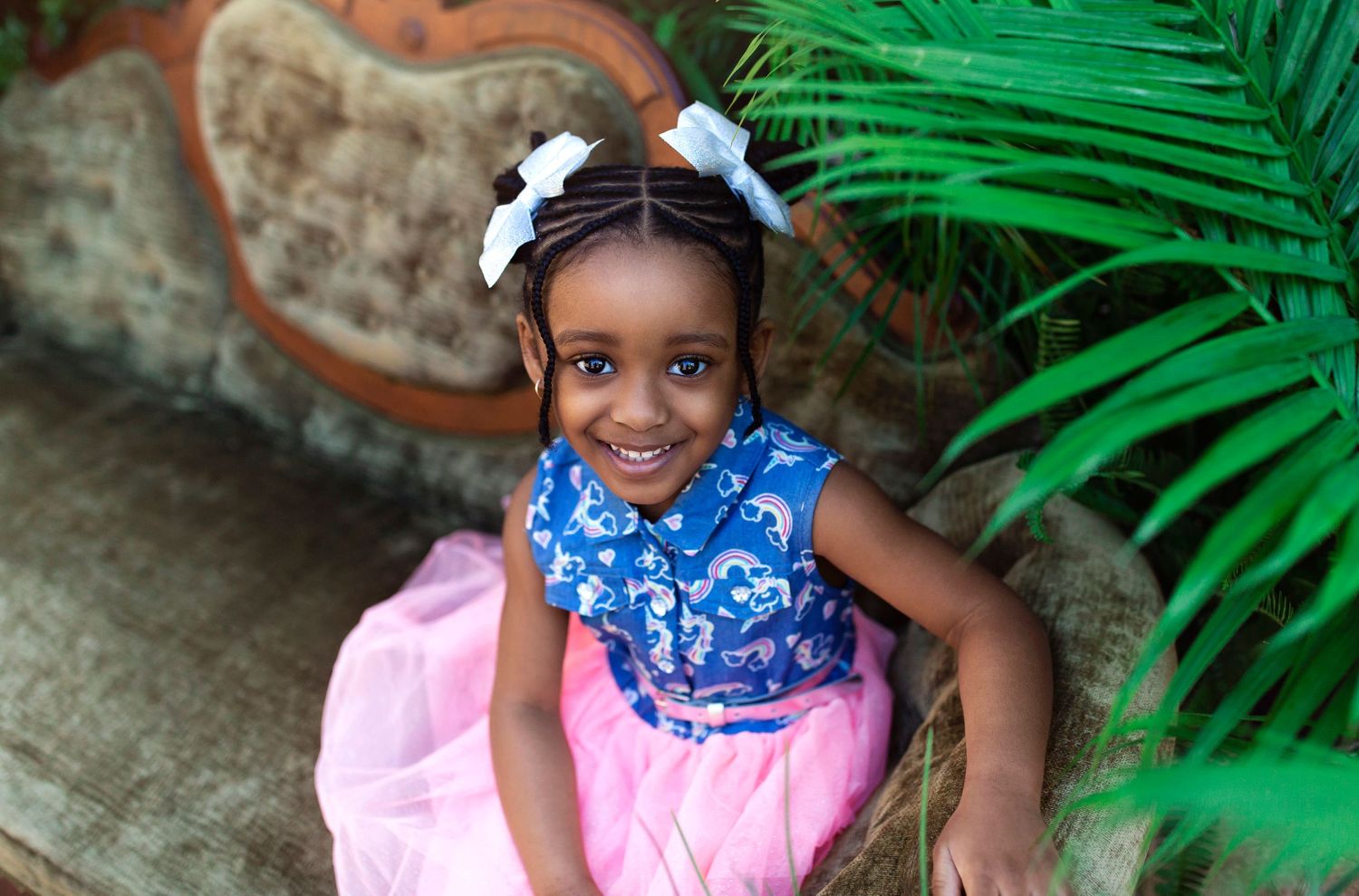 Vibrant outdoor portrait session with palm leaves and vintage furniture.