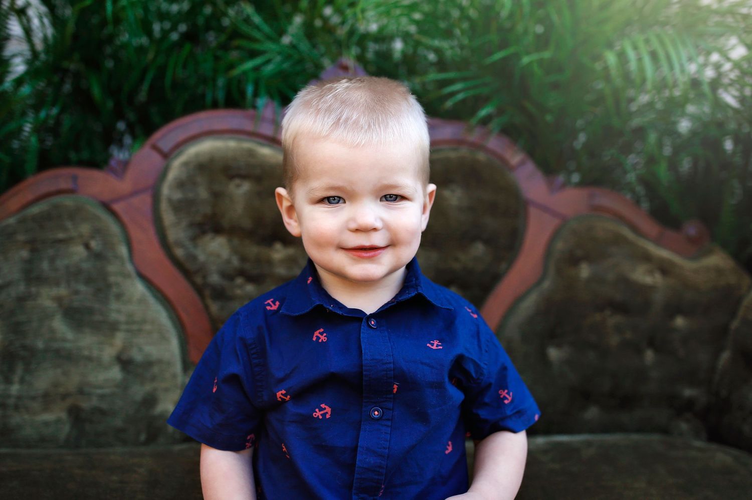 Child in navy polka dot shirt sitting on vintage couch with green plant background.