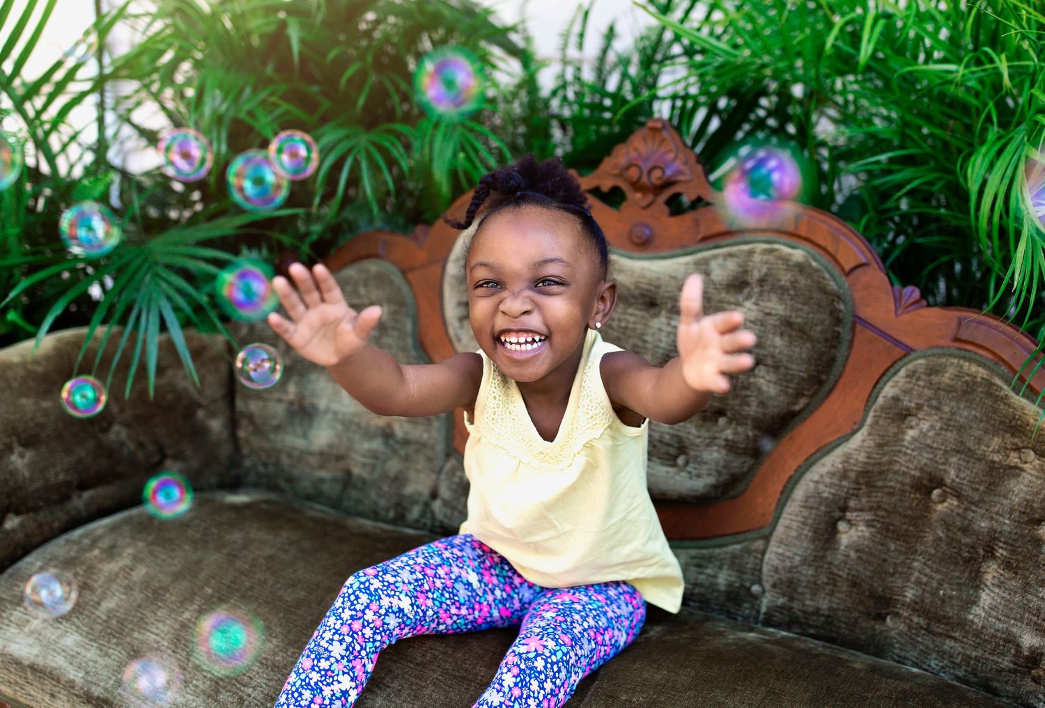 Kids playing with bubbles and having fun on stone furniture in a tropical garden setting.