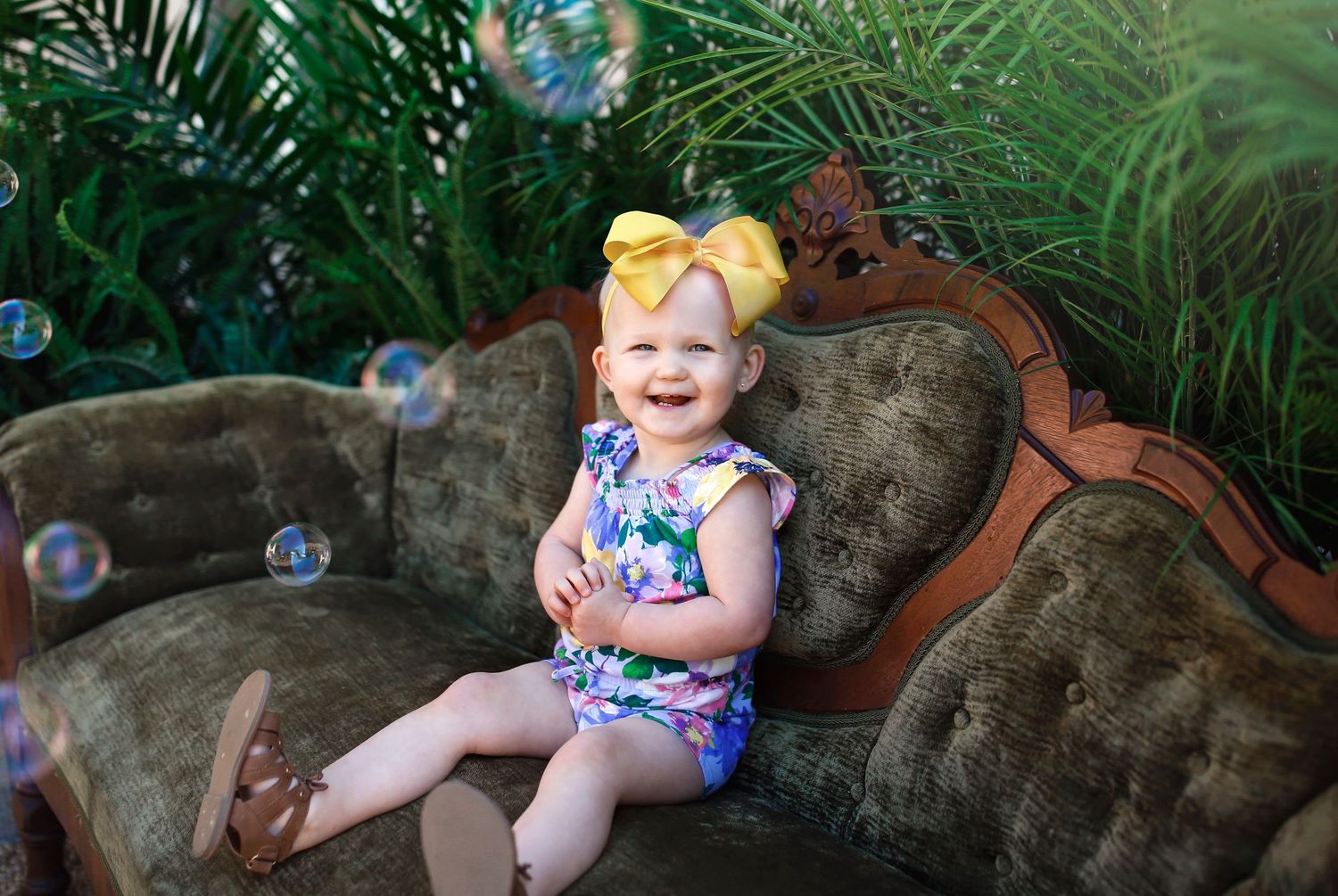 Playful photo session on a vintage tufted couch outdoors with lush tropical plants in the background.