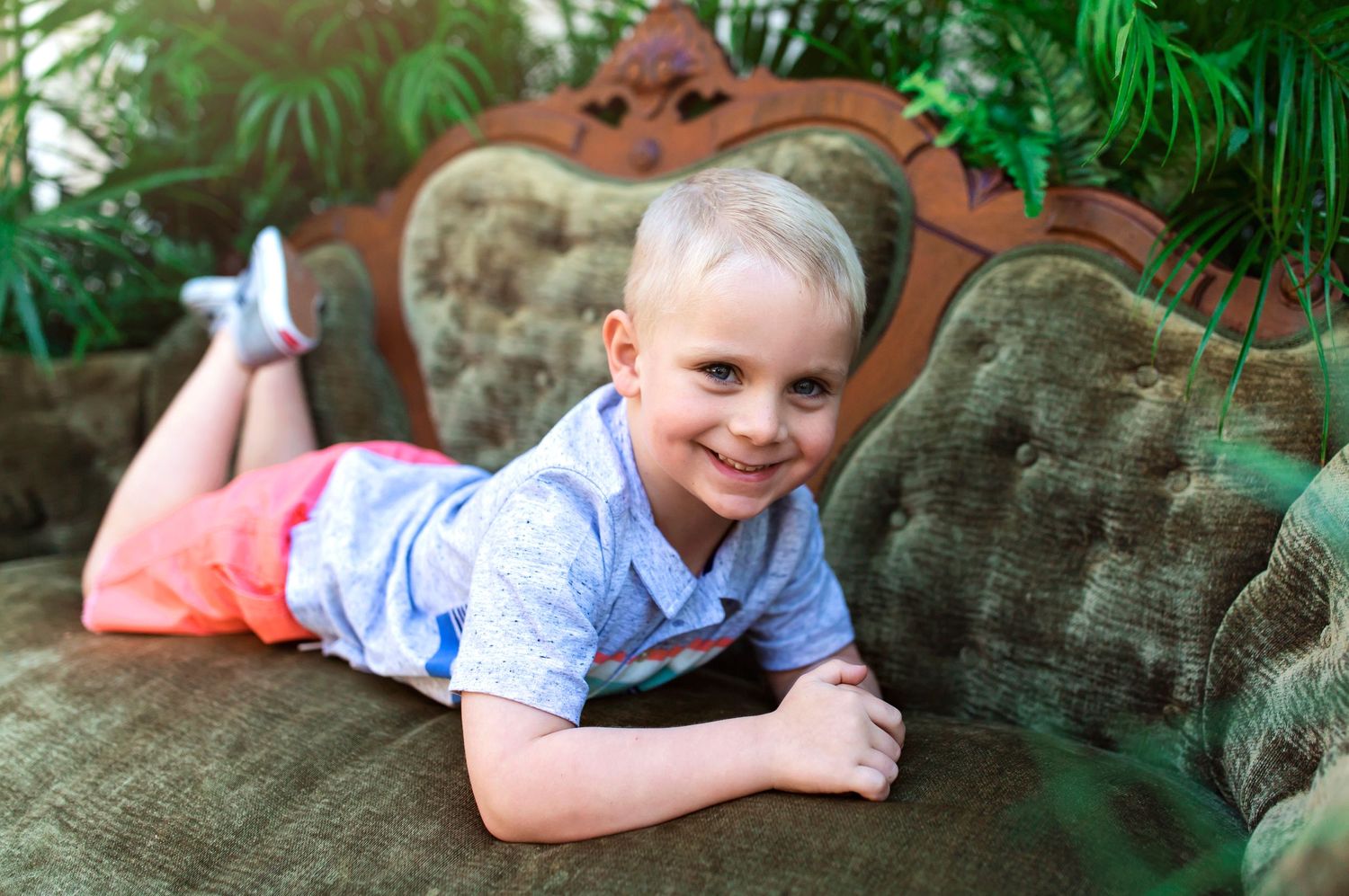 Outdoor photography session with vintage tufted couch and tropical palm backdrop.