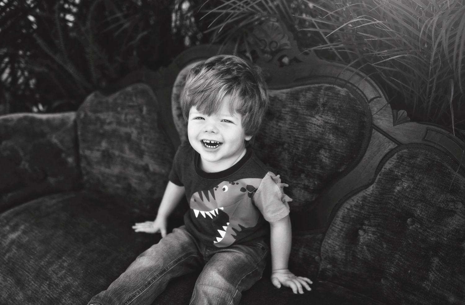 Black and white portrait of joyful child sitting on vintage velvet couch.