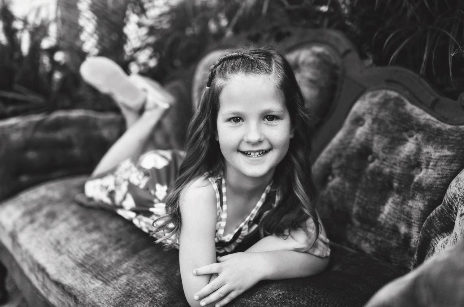 Black and white image of child posing playfully on vintage couch.