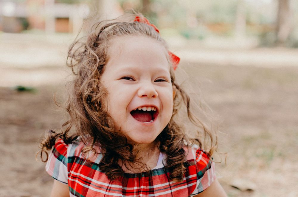 A joyful expression captured in close-up with curly hair and a red plaid dress.