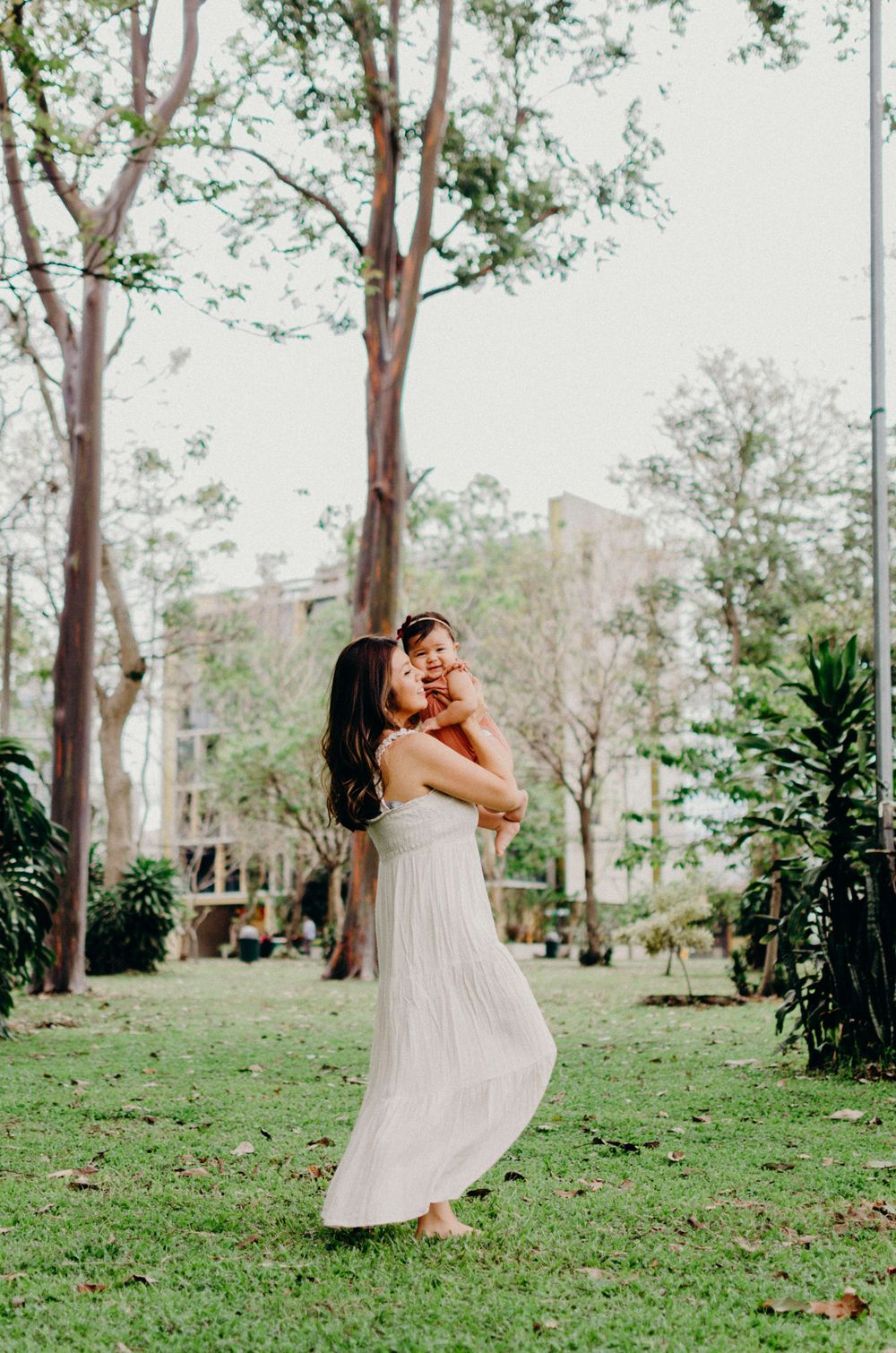 A white-dressed figure twirls with joy in a sunlit park surrounded by tall eucalyptus trees.