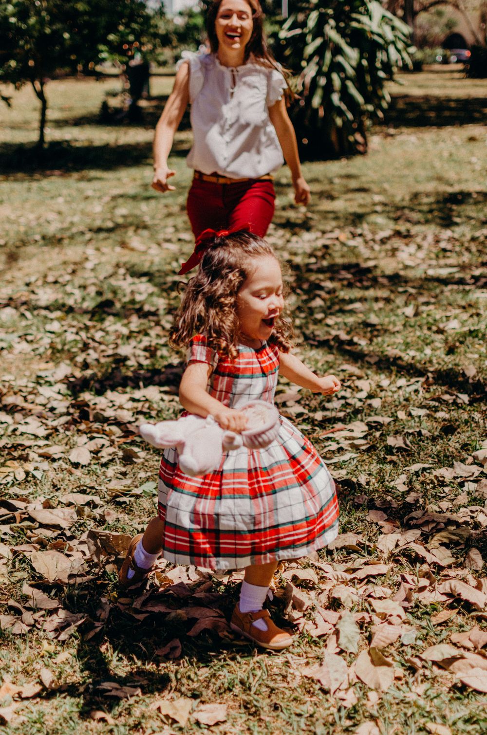 A playful chase through fallen leaves in a park with a plaid dress swirling in motion.