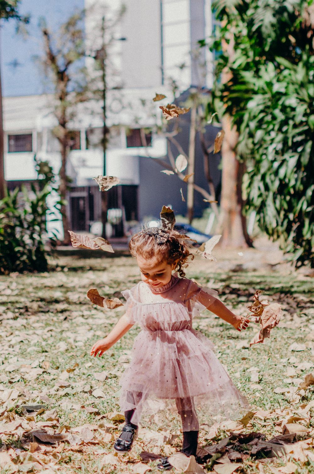 A child in a pink tulle dress dances joyfully among falling autumn leaves.