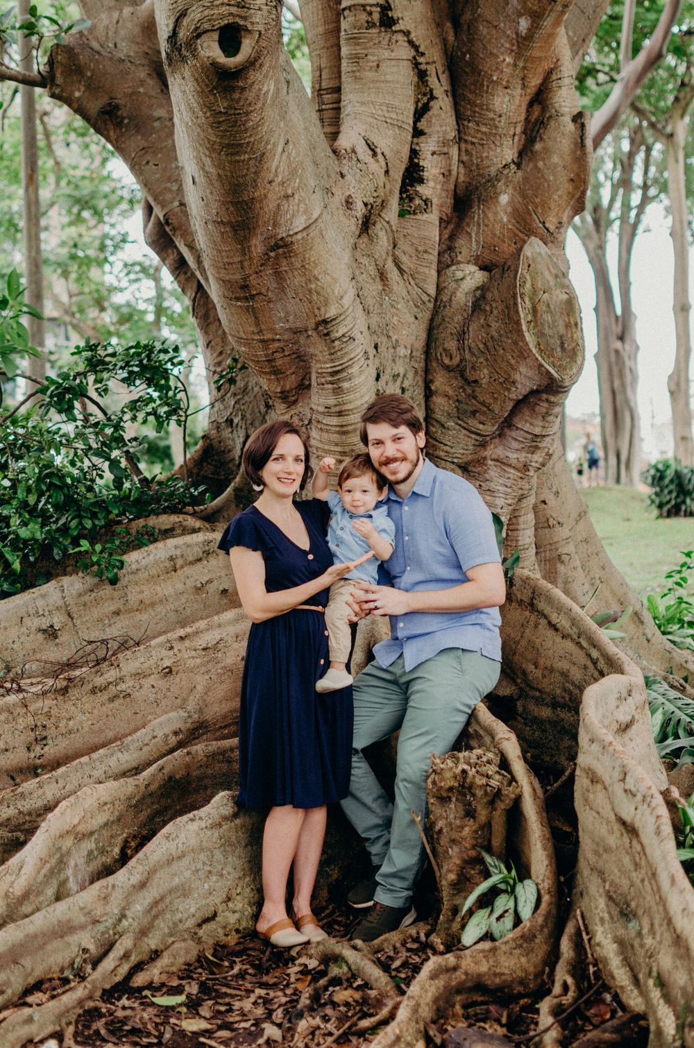 A family portrait taken against a magnificent tree trunk in a serene park setting.
