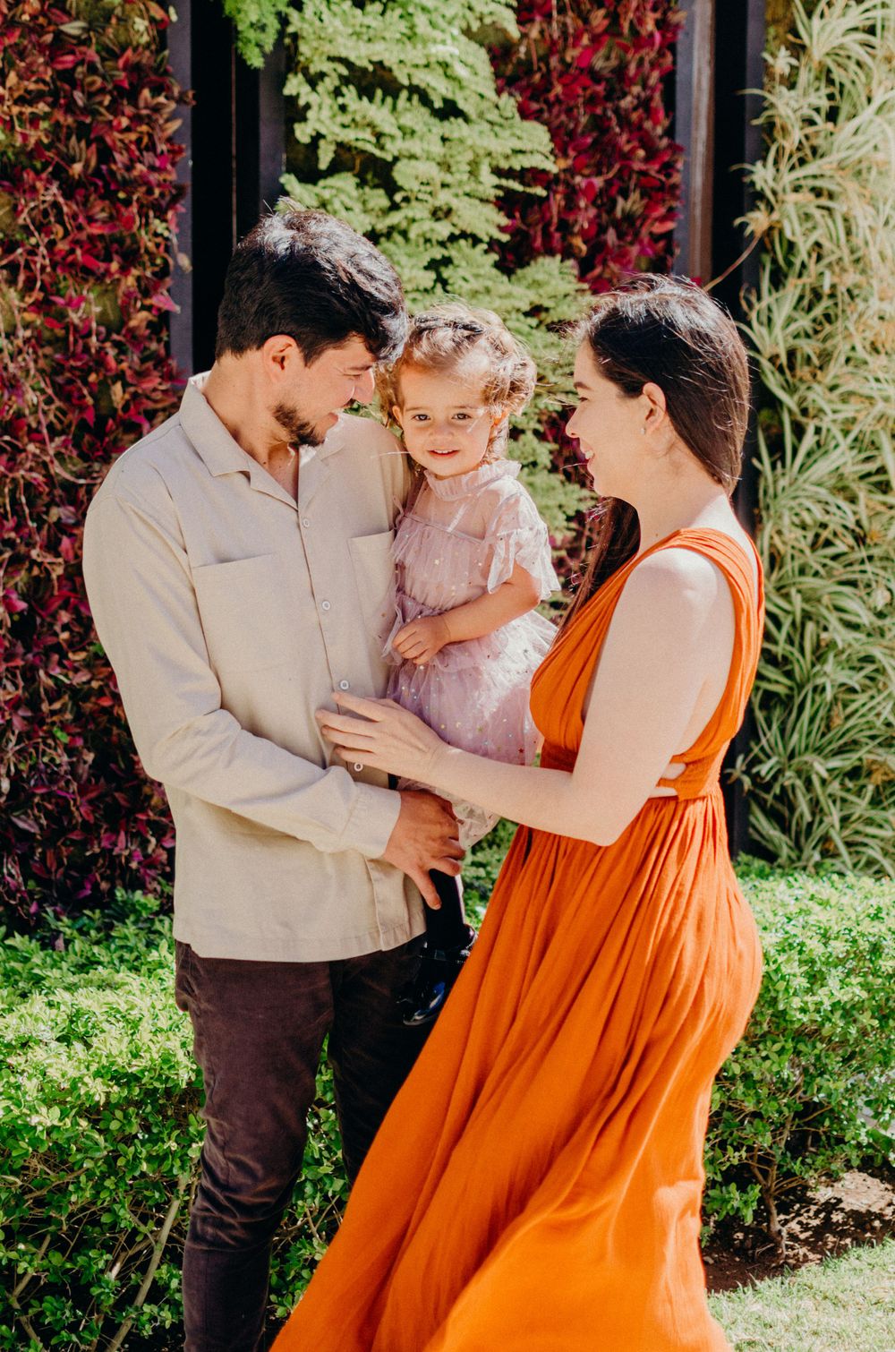 A tender family moment shared in a garden with vibrant red foliage in the background.