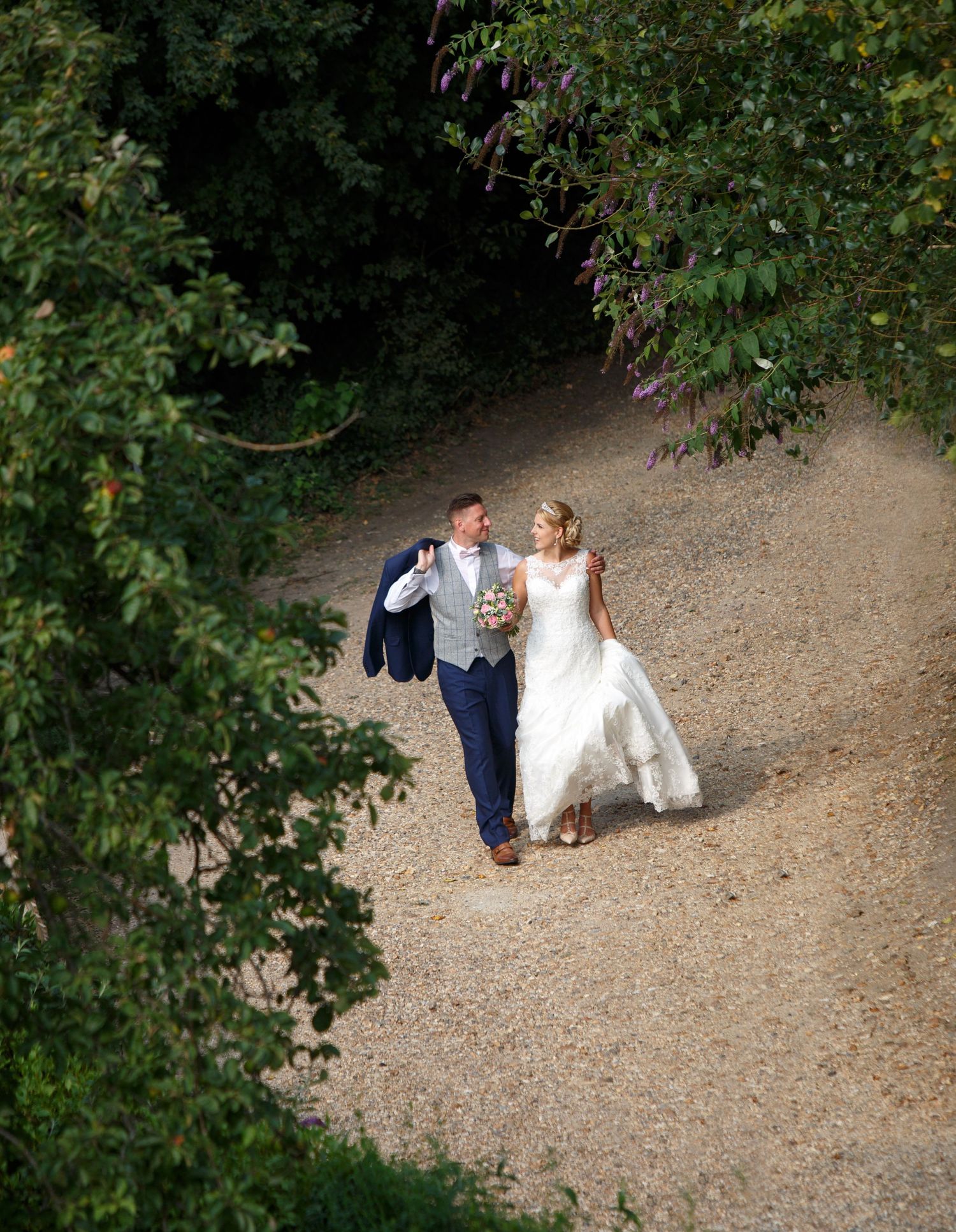 A couple strolls along a winding garden path surrounded by lush greenery.