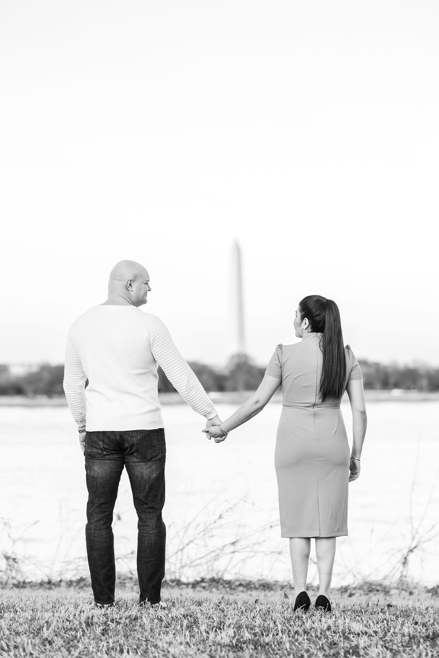 Black and white photo showing a couple holding hands while standing together in a grassy field.
