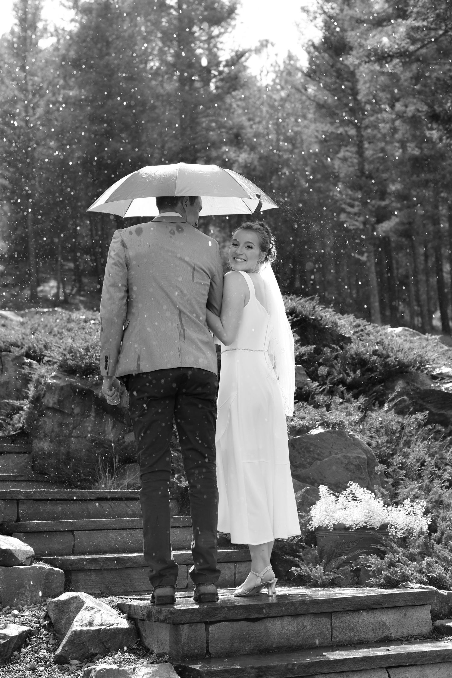 A vintage black and white photo of figures with umbrellas standing on wooden planks in a garden.