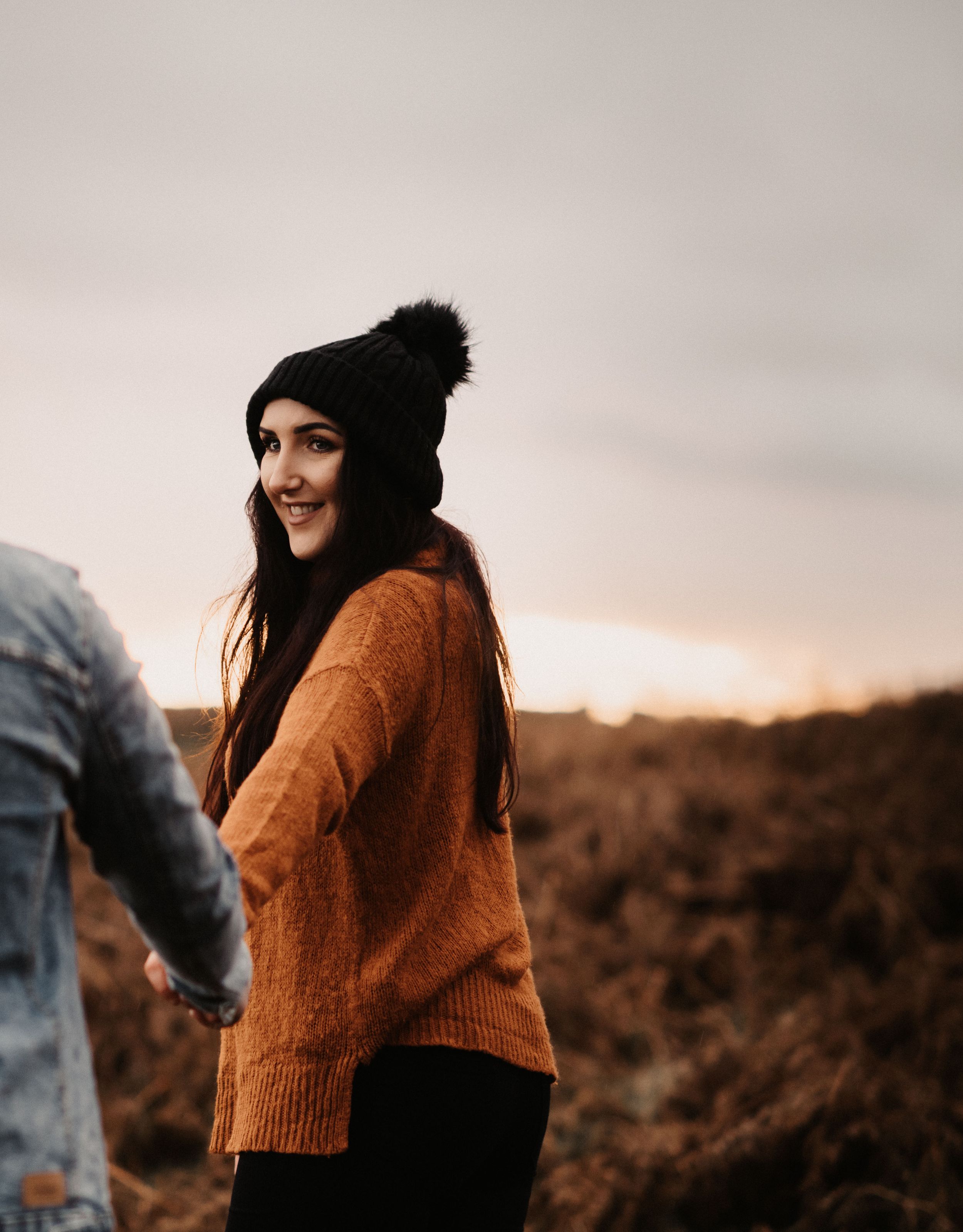 Person in orange sweater and black beanie against sunset backdrop.