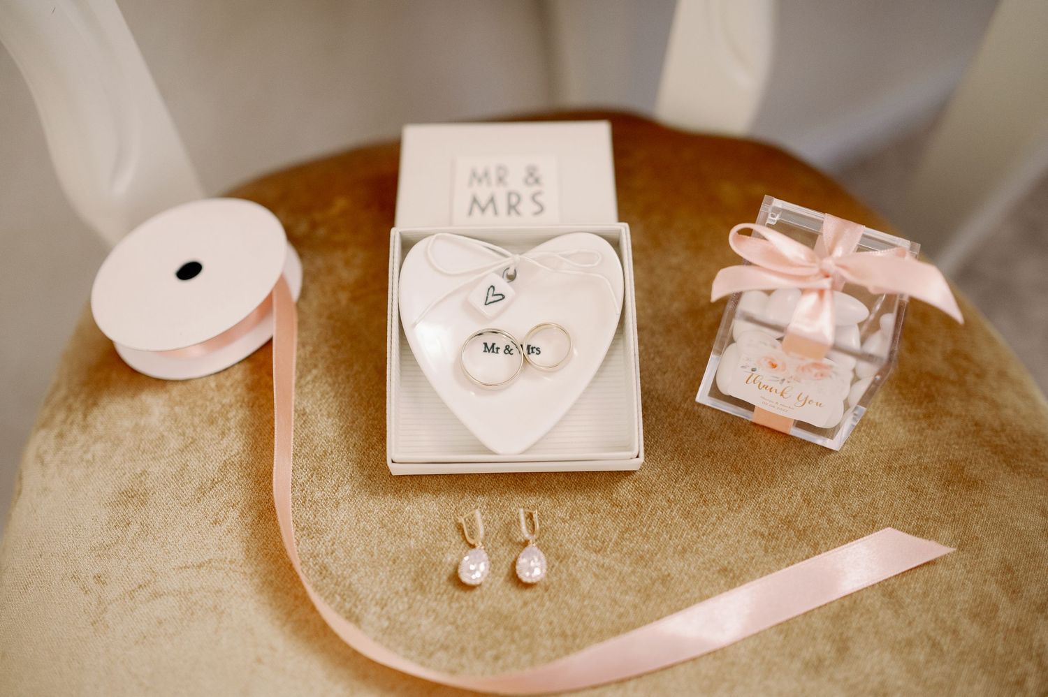 Wedding details including jewelry, ribbon, and Mr & Mrs decor arranged on a golden surface.