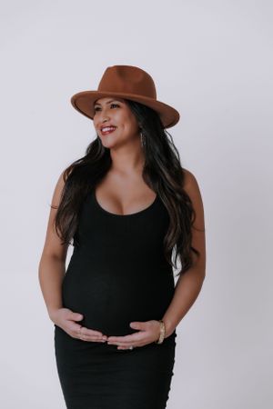 Maternity portrait with brown hat against light background.