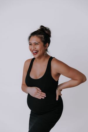 A joyful maternity photoshoot featuring poses in a black tank top against a light backdrop.