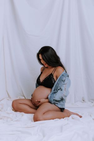 Maternity photoshoot against white backdrop with denim jacket.