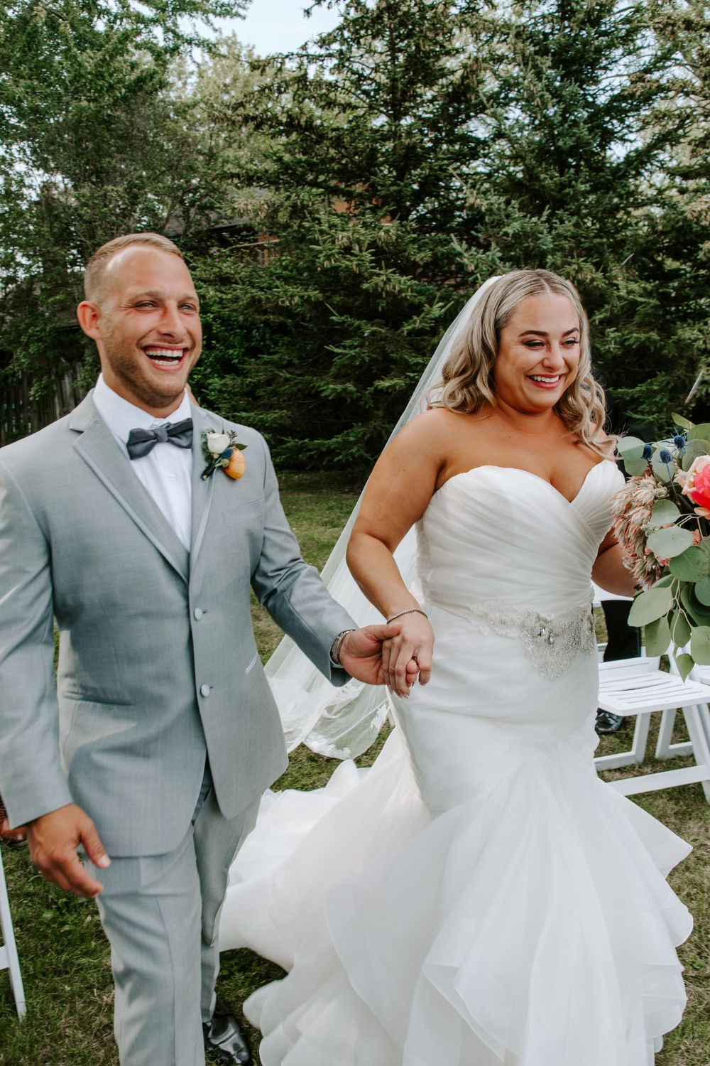 Joyful newlyweds walk hand in hand after outdoor wedding ceremony.