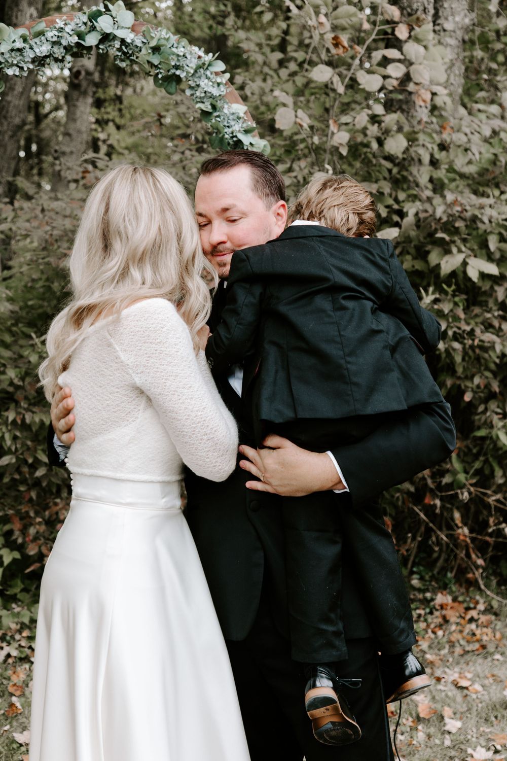 Wedding couple shares joyful moment with child in outdoor garden setting.