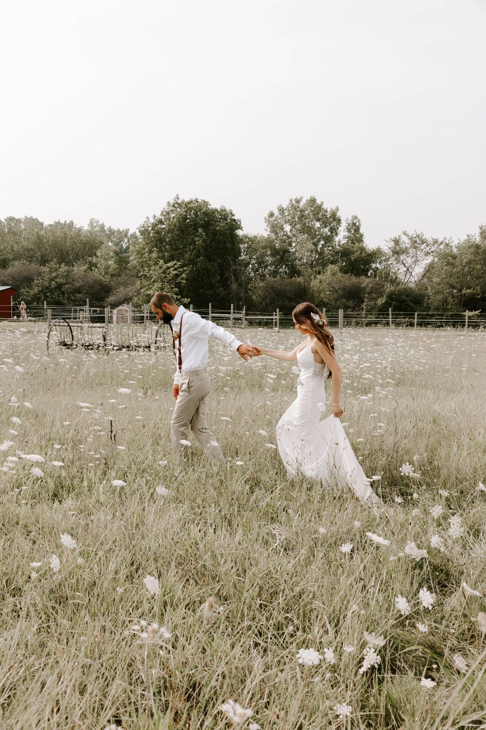 Playful couple running through sun-drenched field with flowing wedding dress.