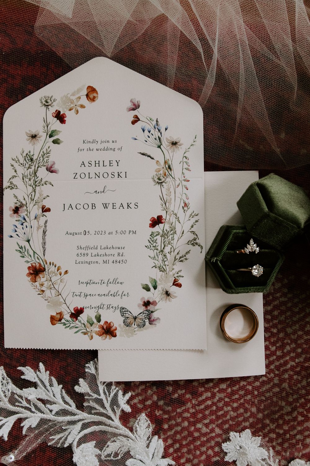Floral wedding invitation with engagement ring and ring box on textured background.