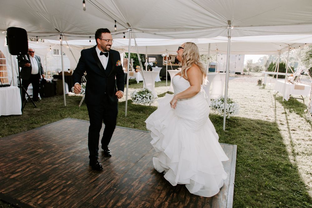 Newlyweds dancing together under white tent on outdoor wooden dance floor.