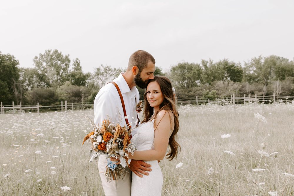 Rustic wedding portrait with autumn bouquet in sunlit meadow.