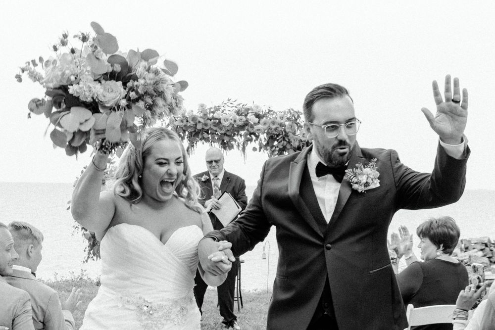 Joyful celebration moment during outdoor wedding ceremony with flower arch backdrop.