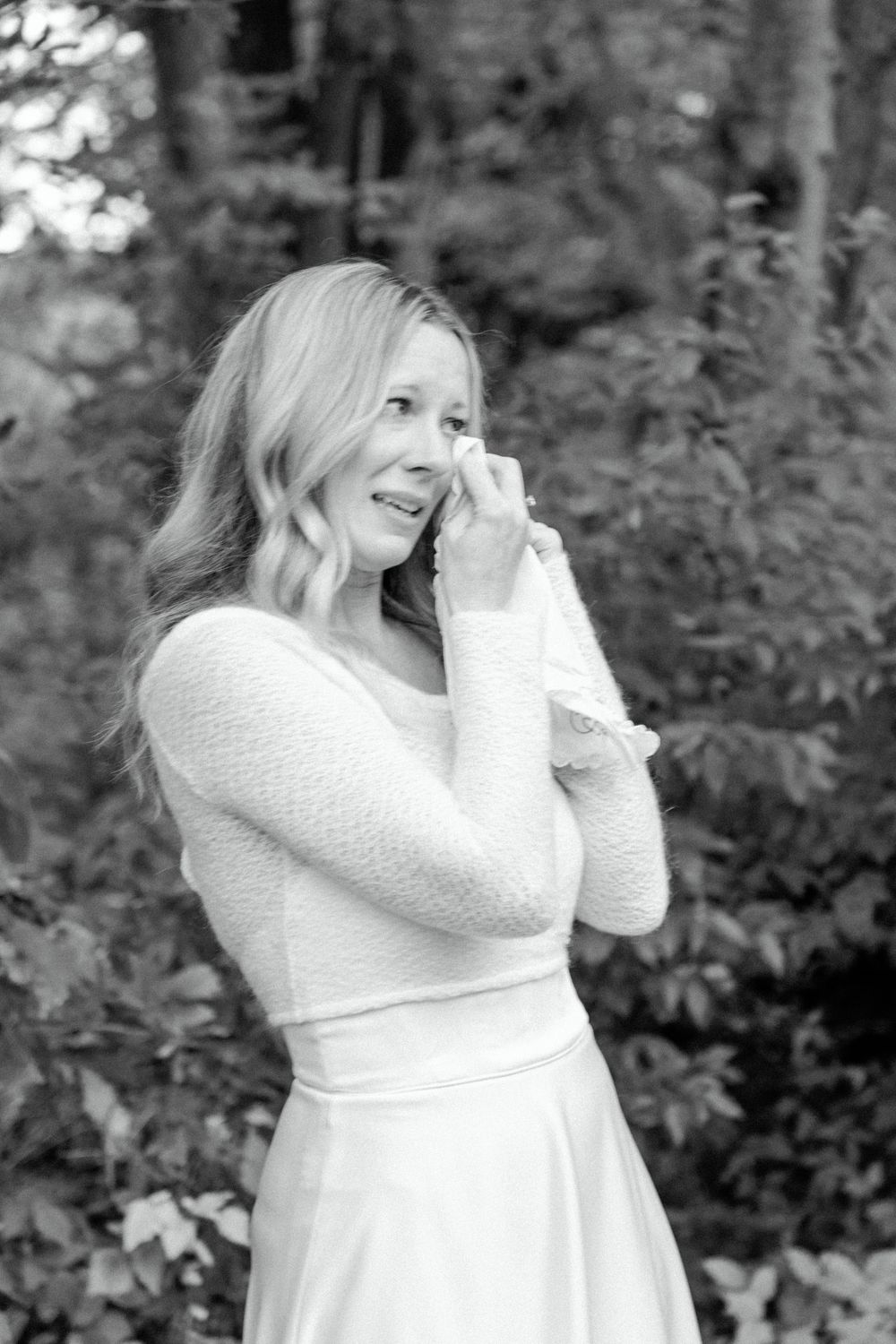 Emotional bride in white dress wipes tears during outdoor wedding photo session.