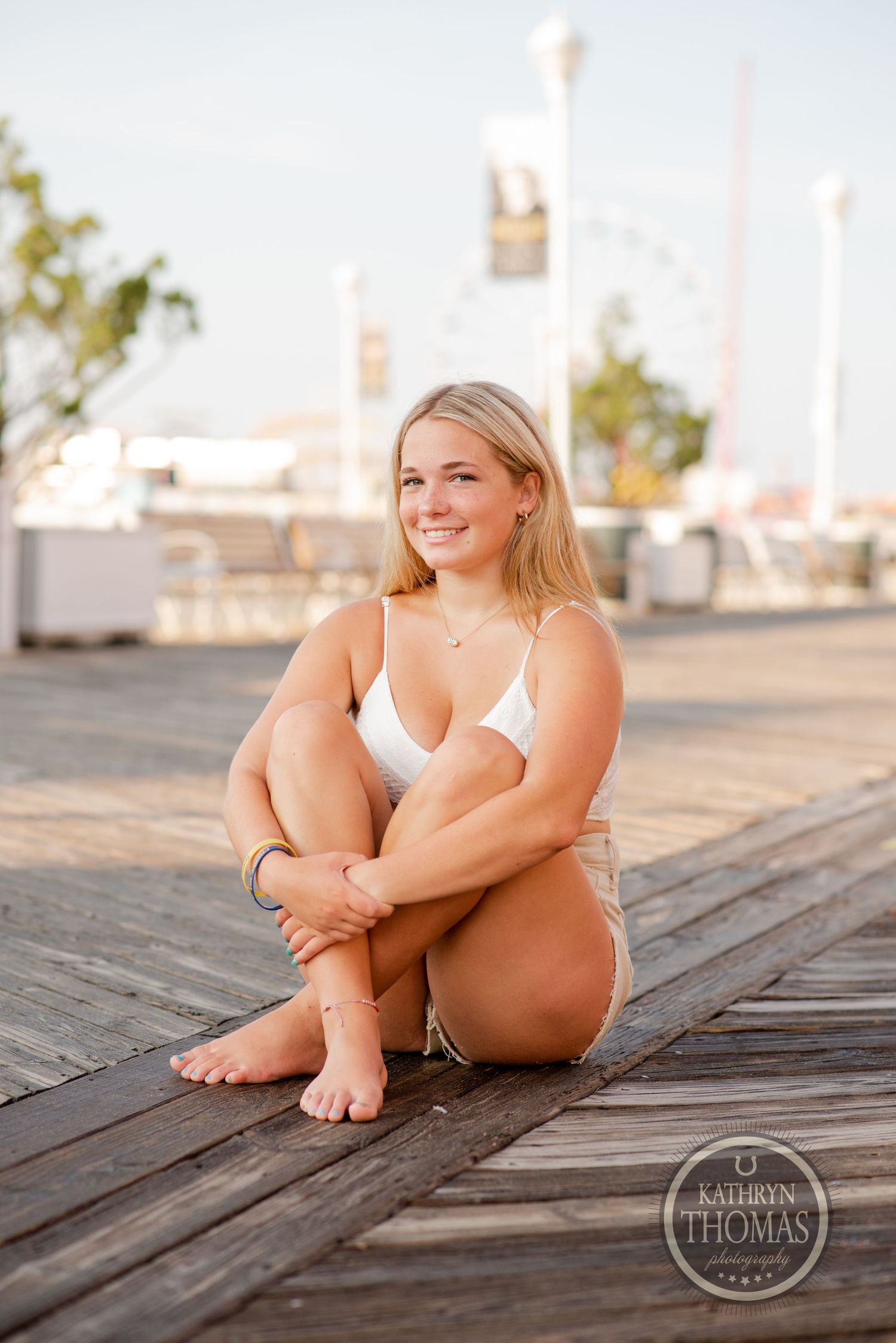 Sunset portrait on a wooden boardwalk with coastal architecture in the background.