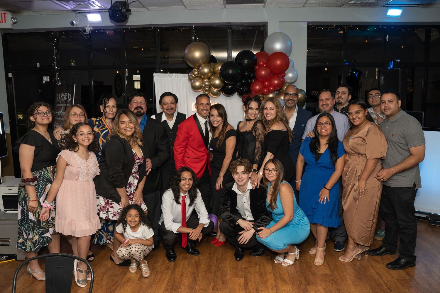 Wide shot of party guests gathered under decorative balloons and lighting.