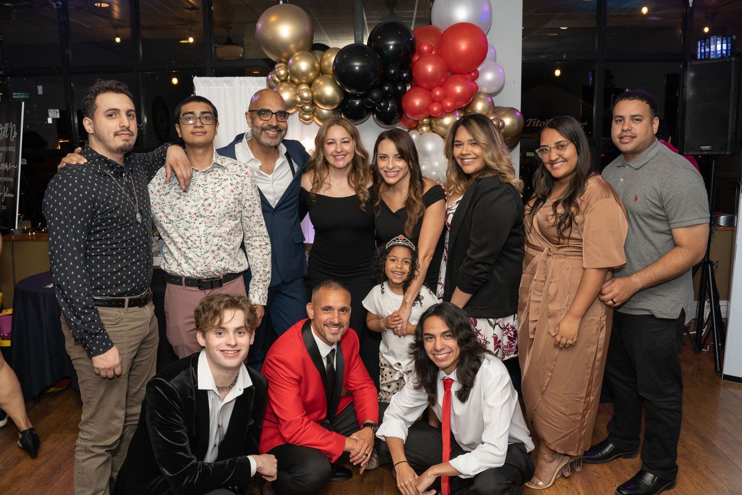 Large group gathering at indoor party with festive balloon decorations.