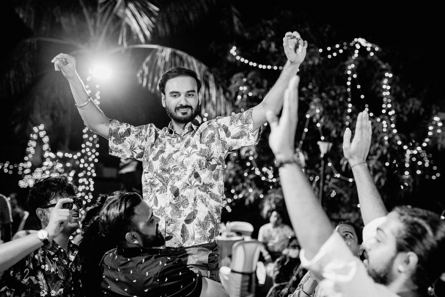 Nighttime celebration with string lights and people dancing in joyful atmosphere.