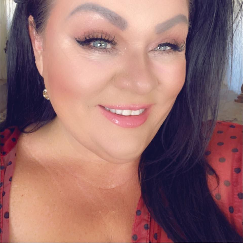 A smiling woman with dark hair and green eyes poses in a red polka dot top.