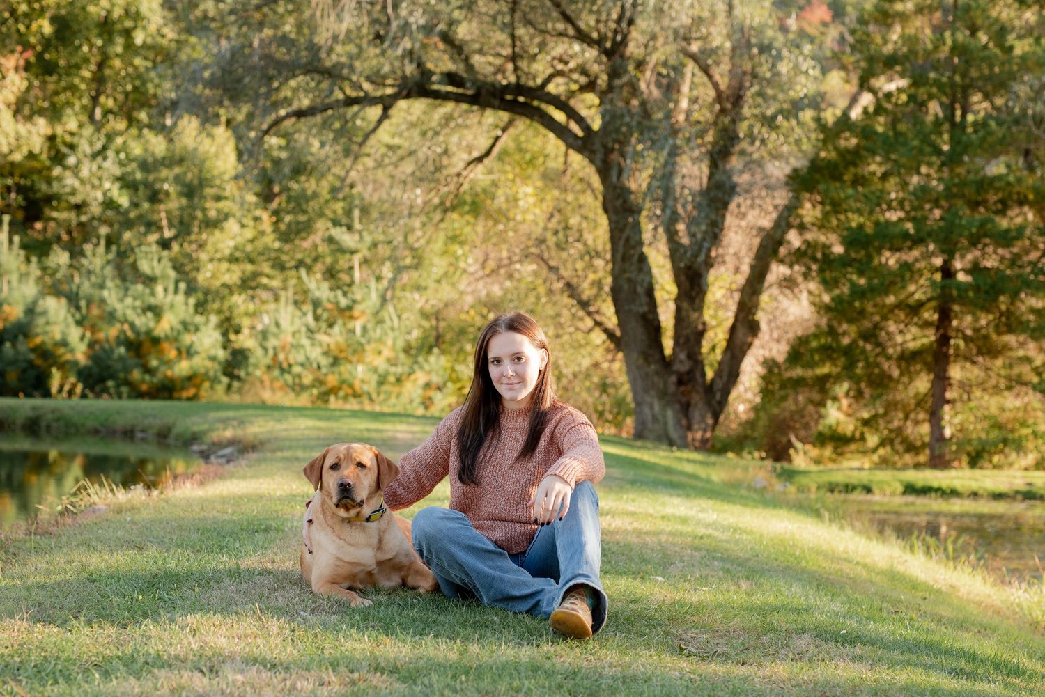 A golden retriever and someone sitting together on grass during a sunny autumn day in a park setting.
