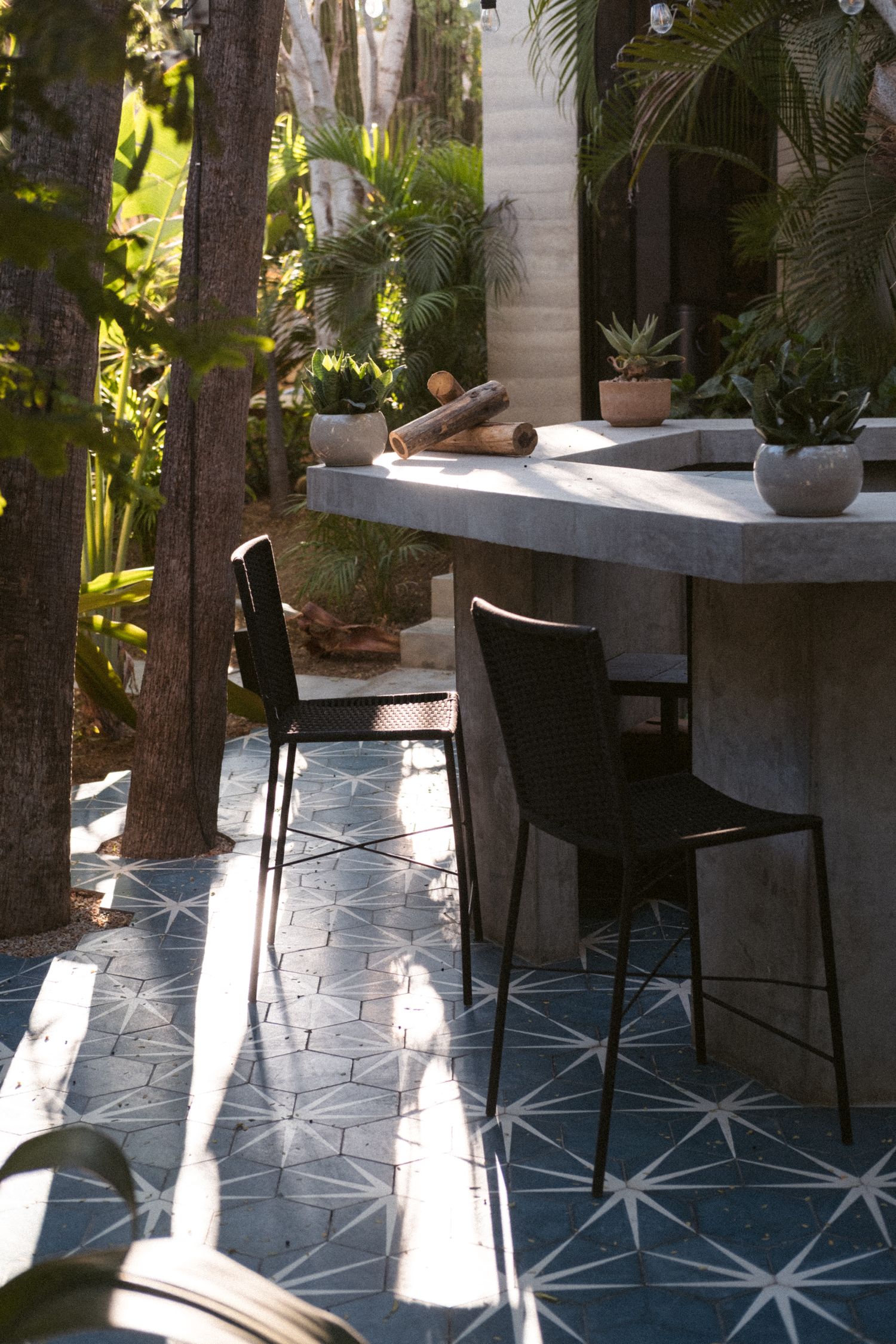 Modern outdoor patio with geometric tiled floor and potted plants on concrete shelving.