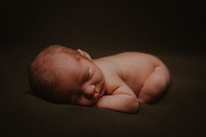 Minimalist portrait of a sleeping baby in dark, moody lighting.