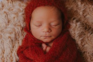 Newborn baby wrapped in soft red knit fabric sleeping peacefully during professional photo session.