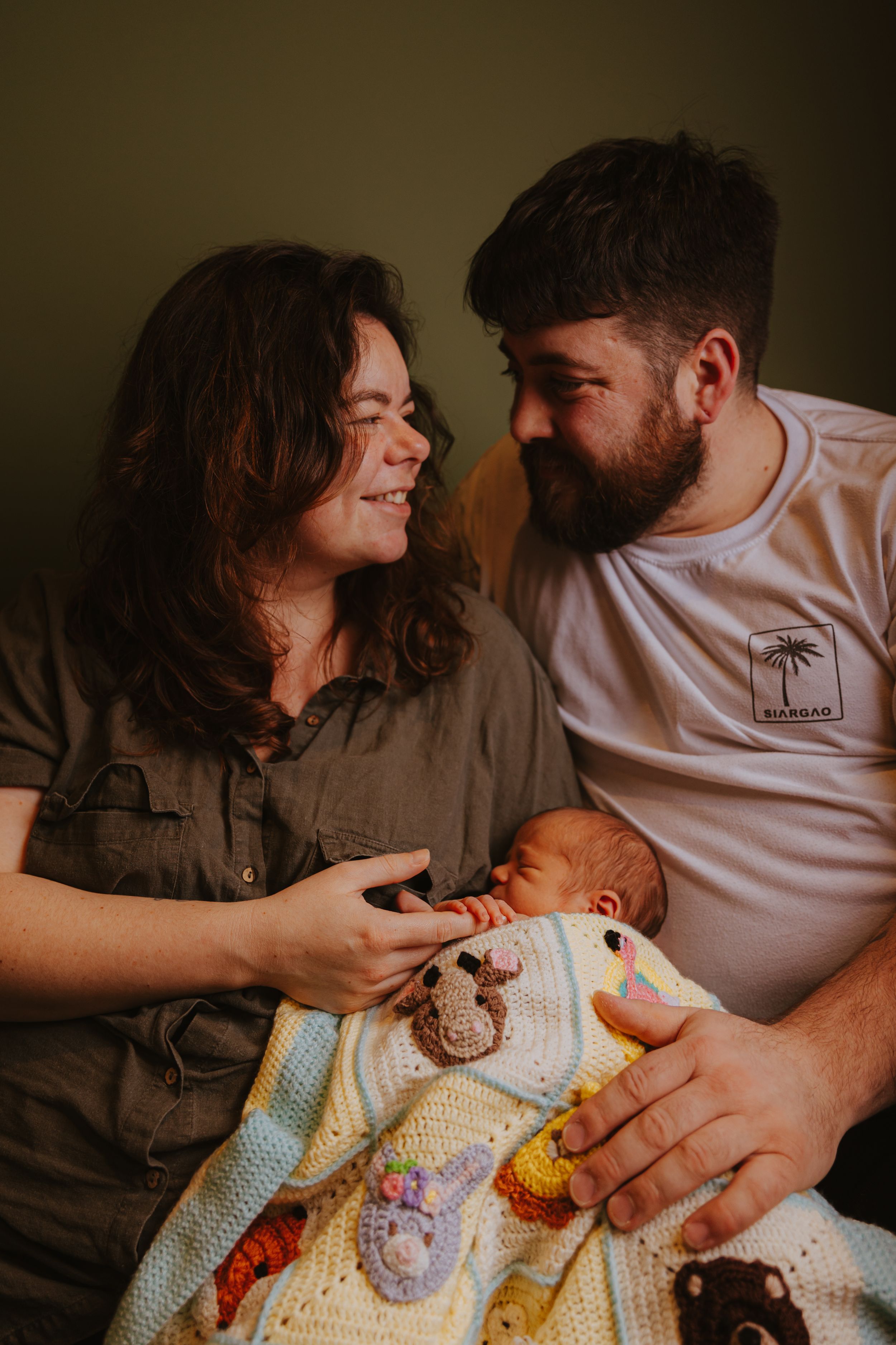 Parents cuddling with their newborn baby on a dark background in an intimate setting.
