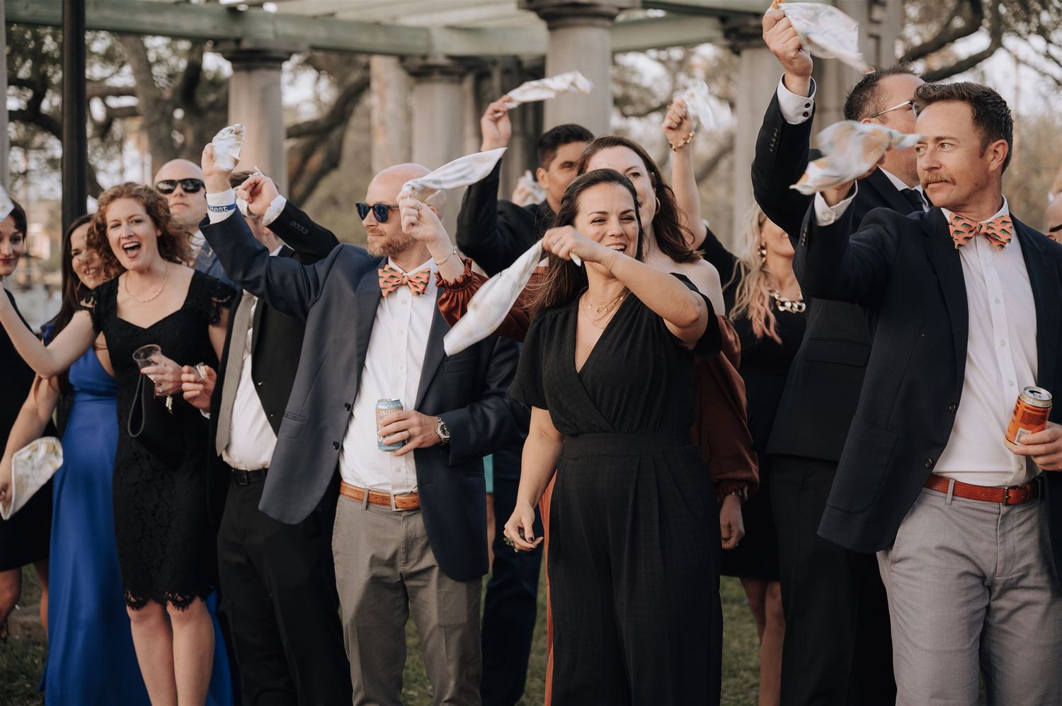 Wedding guests raise their hands in celebration during an outdoor reception.