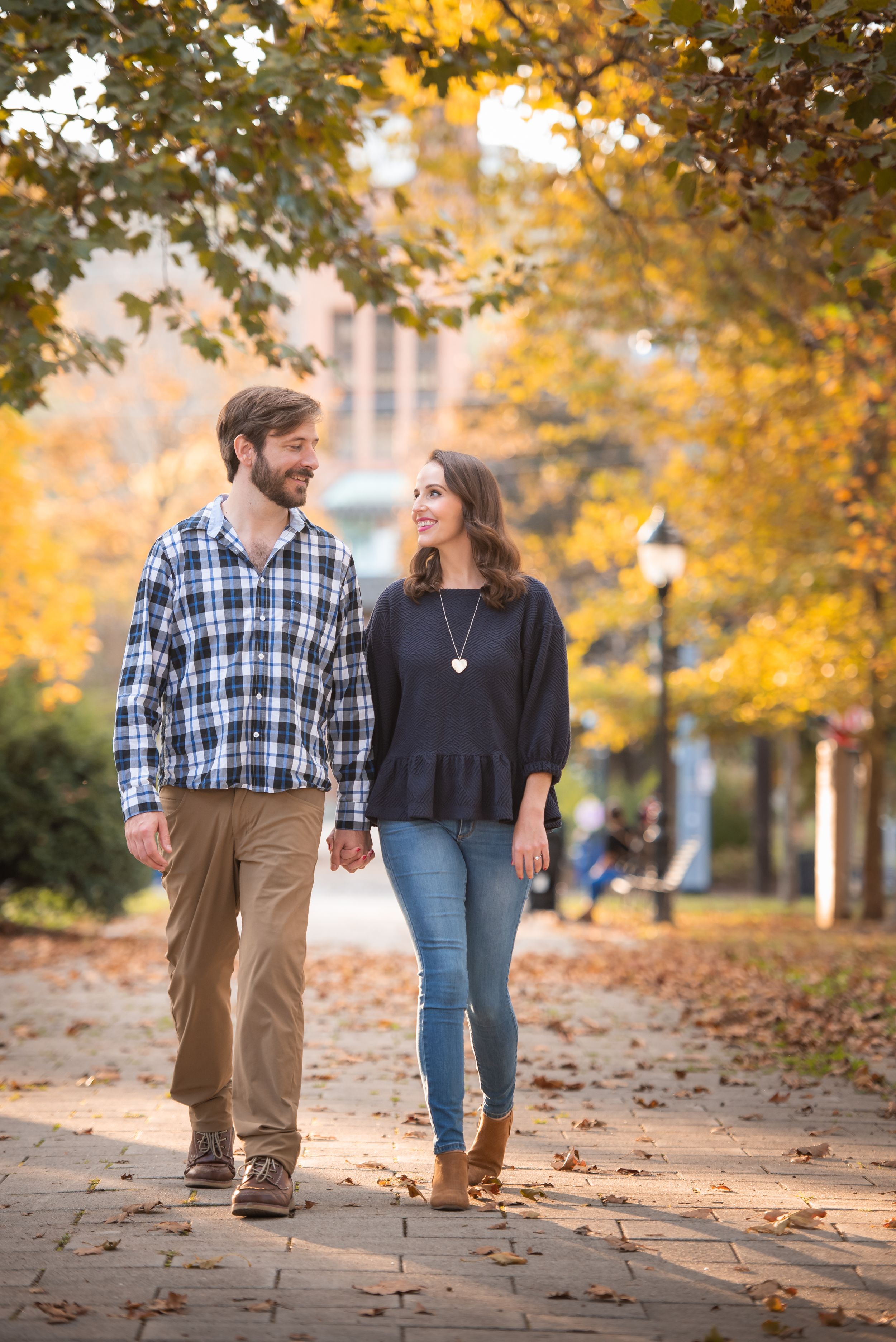 Couple walking hand in hand along a leaf-covered path during autumn.