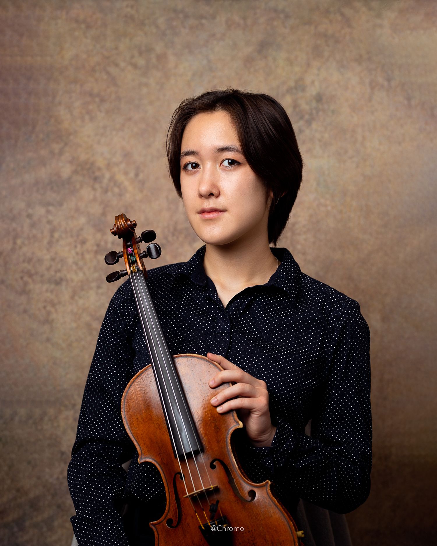 Classical musician in polka dot shirt holding a violin in formal portrait setting.