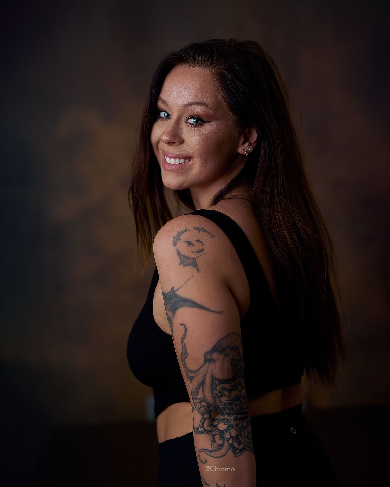 Studio portrait showing detailed arm tattoos against a dark background.