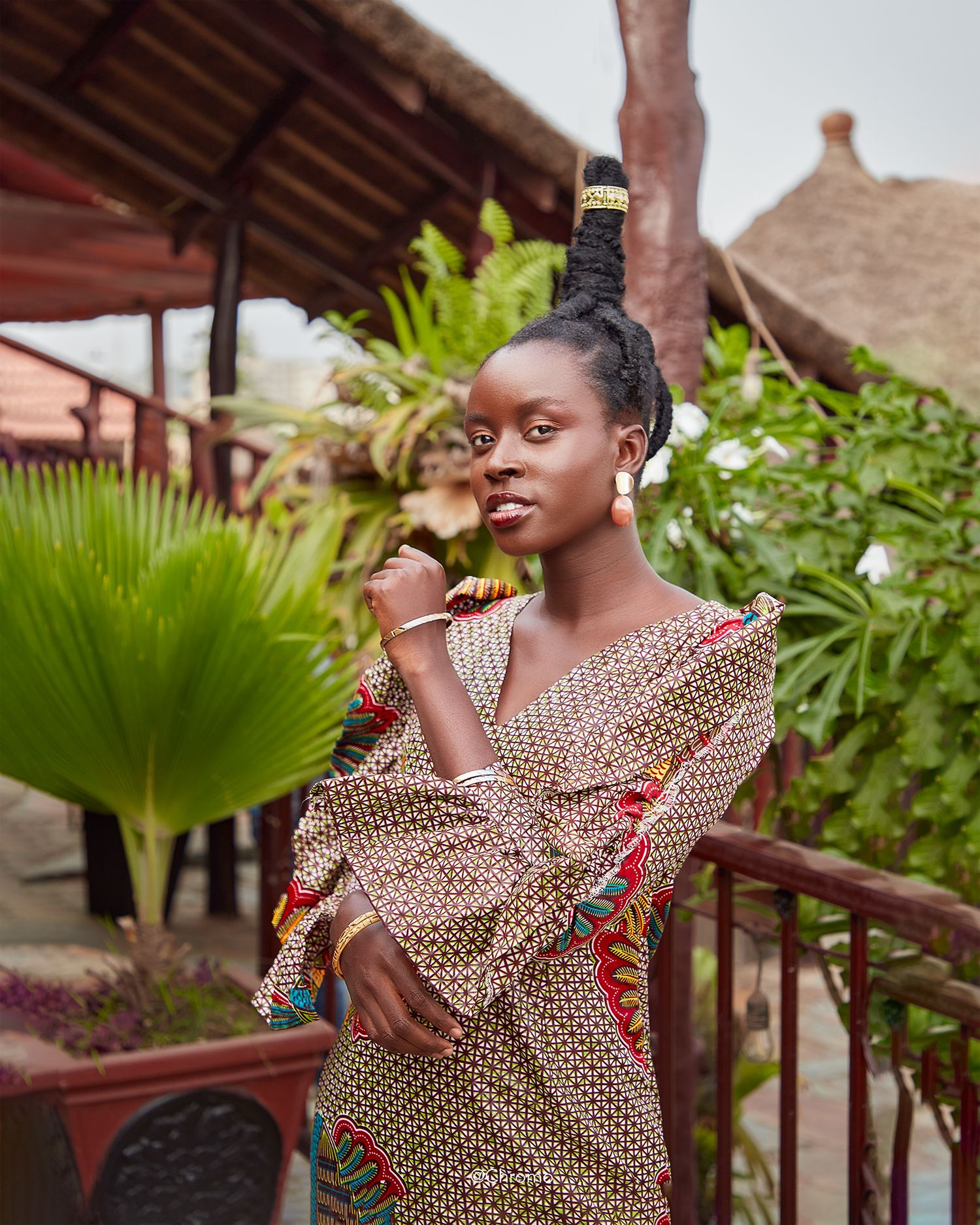 Person in patterned dress poses against tropical garden background with palm fronds.